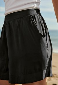 Shorts noirs avec une texture douce, une taille élastique et des poches latérales. Le design comprend une coupe ample et un ourlet droit.