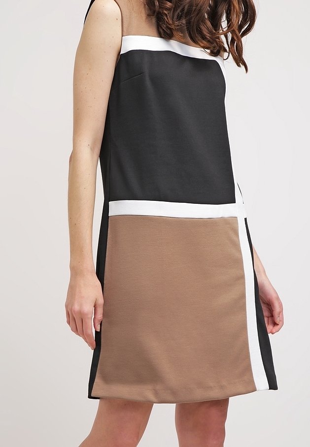 Femme portant une robe sans manches bicolore noire et marron avec une bordure blanche, debout devant un fond neutre uni.