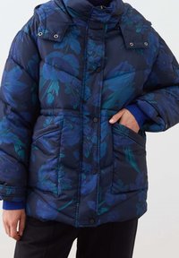 Giacca imbottita blu navy con motivo floreale in tonalità di verde acqua e blu, dotata di colletto alto, bottoni a pressione e tasche frontali.
