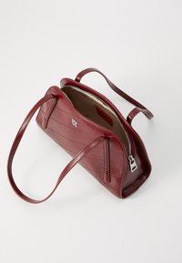 Borsa a mano in pelle borgogna con forma strutturata, chiusura con zip e due manici; presenta cuciture orizzontali e dettagli in hardware con logo.