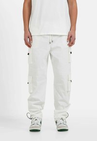 Witte cargobroek met verstelbare trekkoord in de taille, twee zijzakken en twee cargozakken. G gedragen met grijze en groene sneakers.