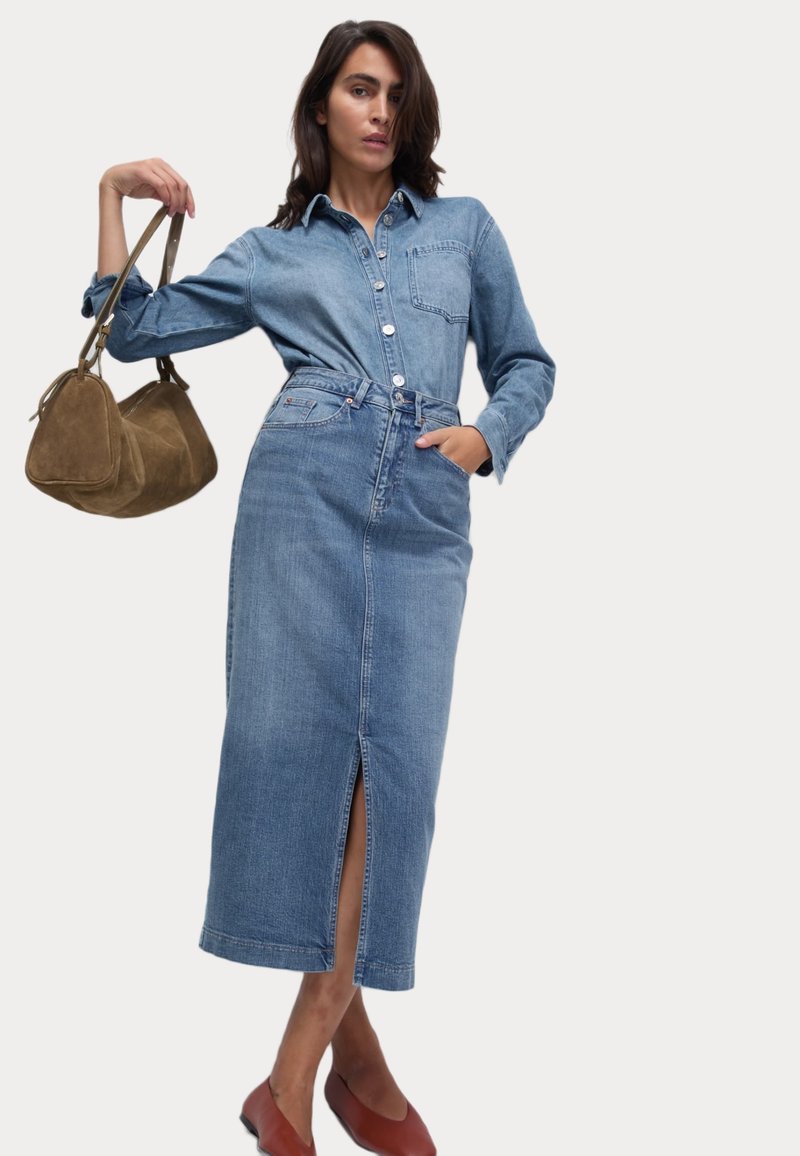 Abito camicia in denim con spacco frontale, chiusura a bottoni e taschino sul petto. Abbinato a una borsa a tracolla in suede marrone e scarpe basse rosse.