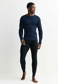 Navy long-sleeve top with ribbed texture and crew neckline, paired with fitted black leggings. Both are streamlined and minimal in design.