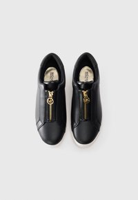 Et par svarte lær slip-on sneakers med gull glidelåser foran og hvite såler, sett ovenfra på en lys bakgrunn.