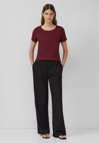 Un t-shirt bordeaux à manches courtes associé à un pantalon large noir, tous deux en tissu doux, présentent une coupe décontractée et des lignes épurées.