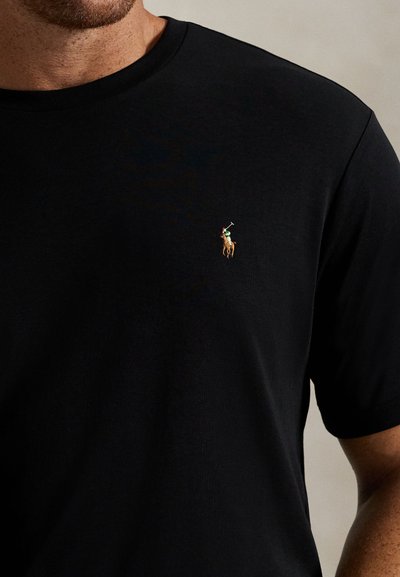 Mann iført en ensfarget svart T-skjorte med liten brodert polo-spillerlogo på venstre bryst.