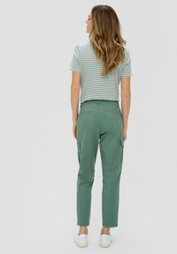 Grüne Cargo-Hosen mit Seitentaschen, schlanker Schnitt und umgekrempeltem Saum, kombiniert mit einem gestreiften kurzärmeligen Hemd. Weiße Schuhe runden den Look ab.