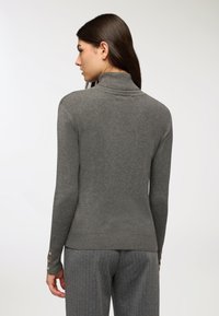 Maglione grigio a collo alto con design aderente. Presenta una texture a costine, maniche lunghe e dettagli con bottoni ai polsini. Tessuto sottile e morbido.