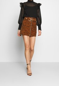 Blouse noire transparente à manches longues avec des accents de volants, associée à une mini-jupe imprimée léopard marron dotée d'une fermeture éclair sur le devant et d'une ceinture.