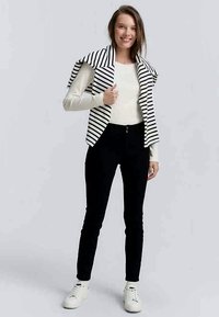 Pantalones negros ajustados combinados con una blusa de manga larga de color crema y un cárdigan de cuello oversized a rayas en blanco y negro. Zapatillas blancas.
