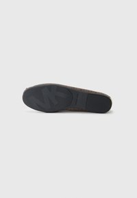 Semelle d'une chaussure plate marron à motifs avec une semelle en caoutchouc noire montrant un grand logo "MK" et la marque Michael Kors.