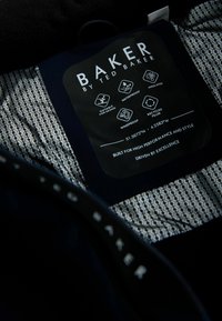 BAKER av Ted Baker etikett inuti mönstrad jacka som visar ikoner för vattentät, isolerad, vindskyddande, återvunnen fyllning, lämplig för skidåkning.
