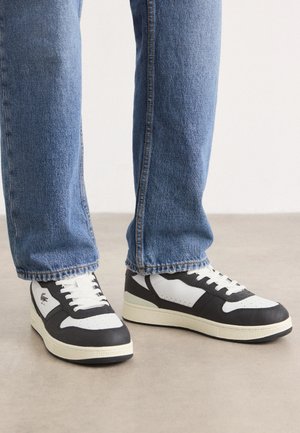 Juodos ir baltos žemos sportinės bateliai su tekstūruotu viršumi, perforuota nosimi, baltais raišteliais ir kreminės spalvos padu.