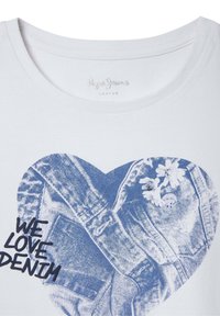 Balta medvilninė marškinė su mėlynos širdies grafika, kurioje yra džinsiniai tekstūrai, gėlių detalės ir užrašas „MES MYLIJAME DŽINSĄ“ juoda spalva.