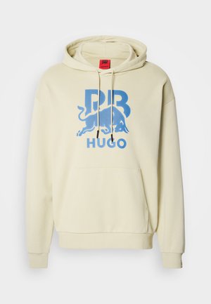 Krämigliten beige hoodie gjord av mjukt tyg, med en stor blå grafisk design av en tjur och texten "PB HUGO" på framsidan.