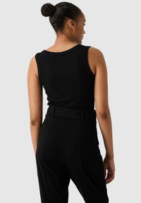 Débardeur noir à côtes avec des bretelles larges, associé à un pantalon noir taille haute, vue arrière montrant un tissu lisse et une coupe ajustée.