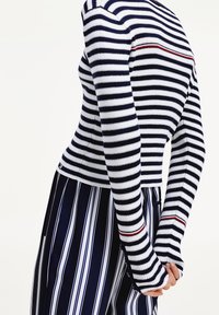 Dlouhý rukáv žebrovaný top v námořnické modři a bílé s červenou akcentní linií, doplněný kalhotami s vertikálními pruhy.