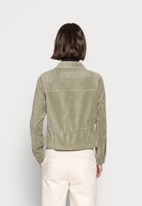Corduroy jacket in muted olive green, featuring a collared neck, fitted silhouette, subtle vertical lines, and an elasticized waist.