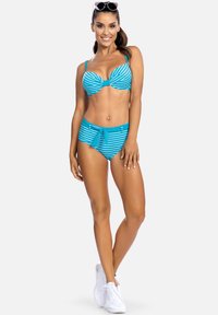 Niebieski i biały kostium kąpielowy w paski, z wyprofilowanym topem i wysokim stanem; zawiera akcent w postaci kokardy z przodu i wykonany jest z teksturowanej tkaniny.