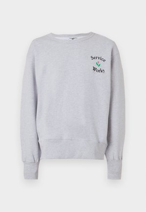 Világosszürke pulóver bordázott mandzsettákkal és szegéllyel, a mellrészen kis fekete "Service Works" felirattal és zöld-rózsaszín virágmotívummal.