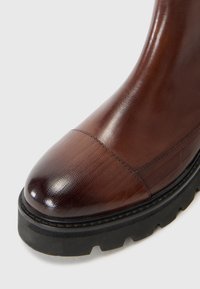 Bottine en cuir marron avec une finition texturée, bout rond et semelle en caoutchouc noire avec un motif de semelle.