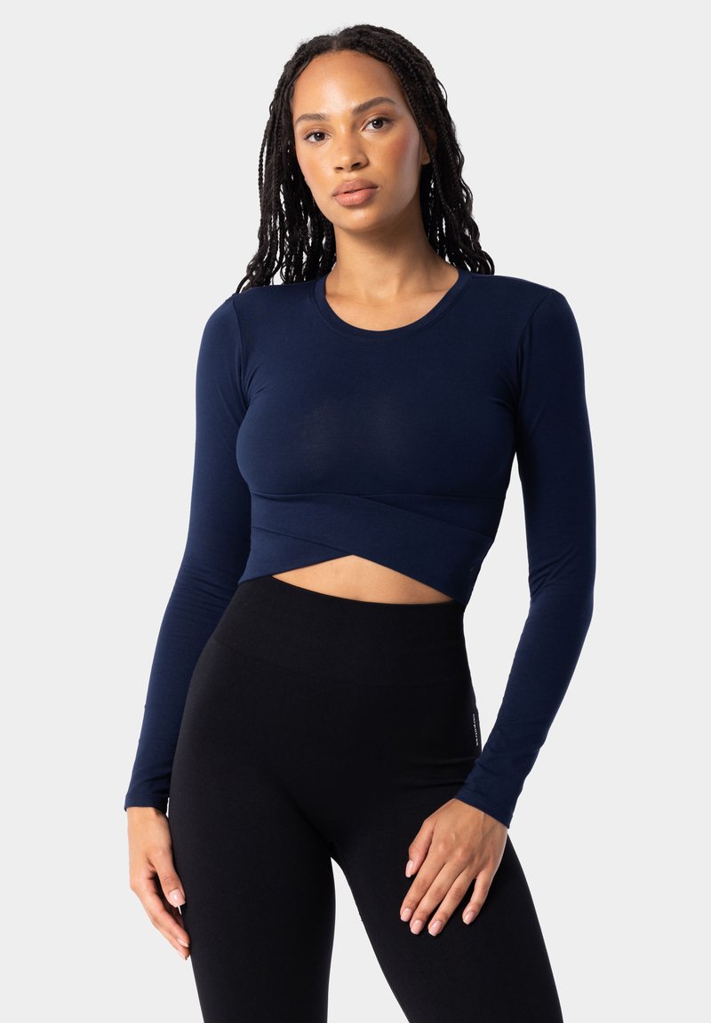 Námornícky modrý krátky crop top s dlhým rukávom, priliehavý strih s okrúhlym výstrihom a prekríženým lemom, kombinovaný s čiernymi legínami s vysokým pásom. Hladká textura.