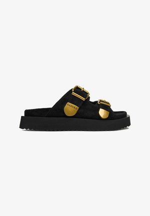Black suede slide sandal with thick sole, two gold adjustable buckles, and "BADURA" logo on side buckle.