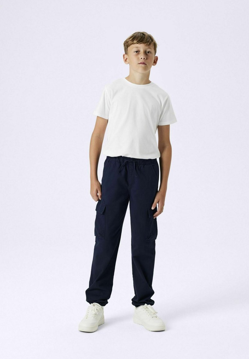 Witte short-sleeve t-shirt gecombineerd met marineblauwe cargo-broek met zijzakken en witte sneakers met een dikke zool.