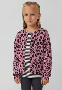 Rosa Strickjacke mit schwarzem Leopardenmuster, ausgestattet mit gerippten Bündchen und Knöpfen. Getragen über einem schwarz-weiß gestreiften Shirt.