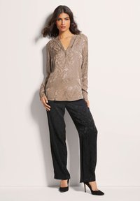 Beige Bluse mit dezentem Muster, V-Ausschnitt-Design; kombiniert mit glänzenden schwarzen Weitbein-Hosen und schwarzen hohen Schuhen. Glatte Stoffstruktur.