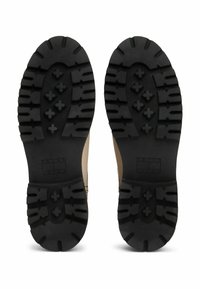 Suola in gomma nera con scanalature pronunciate e motivi incrociati, con una tomaia in pelle marrone chiaro visibile ai bordi.