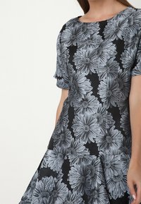 Černé šaty s květinovým vzorem s velkými šedými sedmikráskami. Krátké rukávy a kulatý výstřih s rozšířeným spodním okrajem. Hladká texture látky.