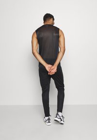 Top de malha sem mangas preto, combinado com calças desportivas pretas ajustadas e ténis brancos com riscas horizontais pretas e detalhes contrastantes.