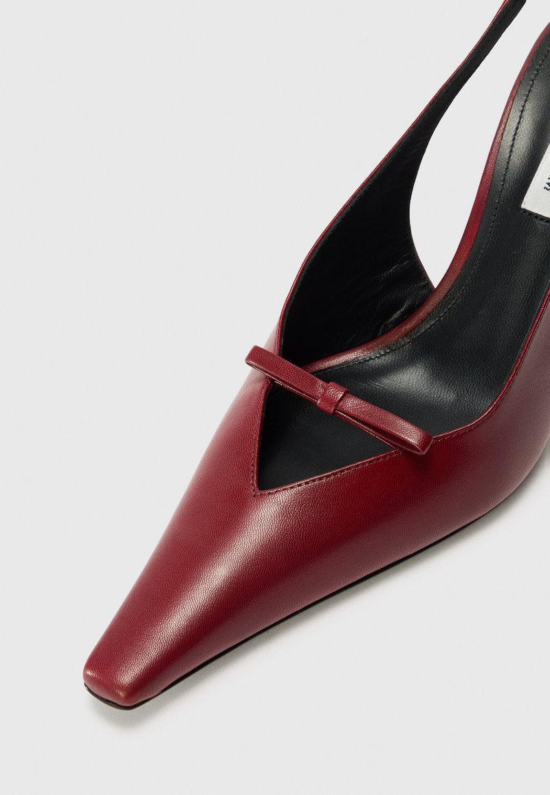 Röd läder slingbackpump med spetsig tå, med en v-formad öppning och ett dekorativt band över framsidan. Svart foder inuti.