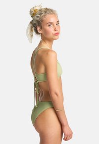 Groene geribbelde bikini met verstelbare bandjes, strikdetail aan de achterkant en een hooggeplaatste onderkant. De stof lijkt glad met een matte afwerking.