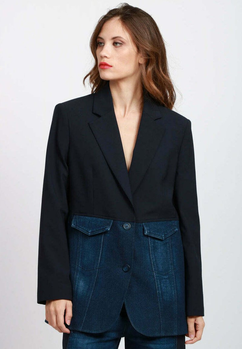 Blazer nero con parte inferiore in denim. Presenta un colletto a revers, due tasche a toppa frontali e una chiusura con due bottoni, con una texture liscia.