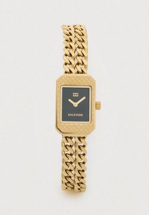 Une montre dorée avec un cadran rectangulaire, un fond noir et une lunette hexagonale. Elle possède un bracelet en chaîne texturé et un logo de marque bien en vue.
