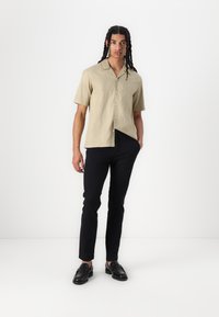 Camisa de manga corta en color beige claro, hecha de una mezcla de lino, combinada con pantalones negros ajustados y mocasines negros, con un corte relajado y cierre de botones.