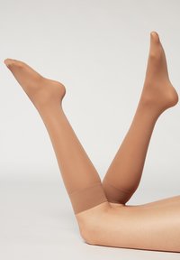 Gennemsigtige, beige lårhøje strømper med en glat tekstur, der har et bredt, elastisk bånd øverst for en sikker pasform.