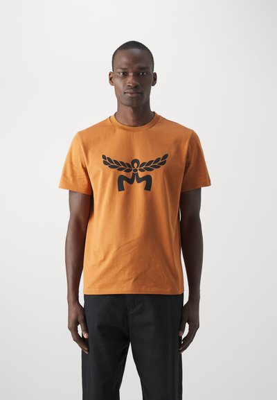 T-shirt en coton orange à manches courtes avec un grand motif graphique noir au centre. Coupe confortable avec un col rond.