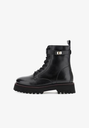 Bota de tobillo con cordones de cuero negro, suela dentada, correa en el tobillo y detalle de hebilla en tono dorado, presentada sobre un fondo blanco.