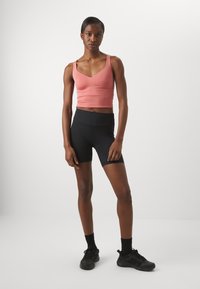 Top corto rosa aderente con spalline larghe, abbinato a pantaloncini da ciclismo neri a vita alta. Tessuto liscio e morbido con design senza cuciture.