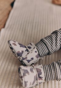 Chaussons en tissu doux à motif camouflage avec un bout arrondi et une fermeture Velcro, associés à des leggings en tissu rayé gris et crème.