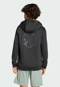 Svart huvtröja med en geometrisk kubgrafik på baksidan, gjord av slätt tyg, med snörning i huvan och ribbade muddarna, tillsammans med ljusa shorts.