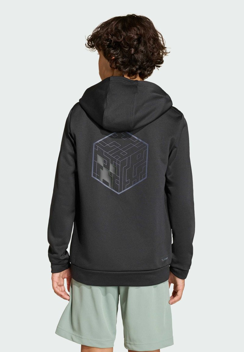 Svart huvtröja med en geometrisk kubgrafik på baksidan, gjord av slätt tyg, med snörning i huvan och ribbade muddarna, tillsammans med ljusa shorts.