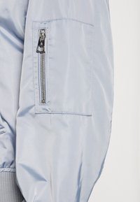 Manche de veste bleu clair avec une poche verticale zippée et des coutures visibles sur un tissu lisse.