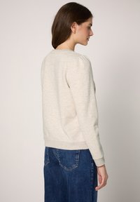 Jasnoszara bluza z okrągłym dekoltem, ściągaczami na mankietach i u dołu, plisami z tyłu oraz miękką tkaniną. Połączona z niebieskimi dżinsami.