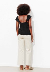 Haut noir sans manches avec bretelles à volants, associé à un pantalon large blanc cassé. La tenue présente un corsage ajusté et une silhouette décontractée.