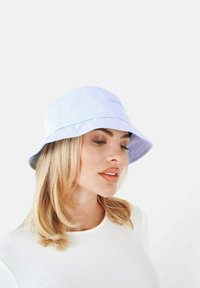Jasnoniebieska czapka typu bucket, wykonana z miękkiego materiału, z przeszywanym rondem i subtelnym logo z przodu. Gładka tekstura i luźny krój.