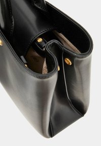 Sac à main en cuir noir avec une forme structurée. Texture lisse, accents en métal doré et intérieur en tissu clair avec un motif subtil.